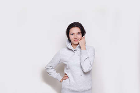 Young woman brunette in a light grey sweater with hood, isolated on white background, looking at camera.の写真素材