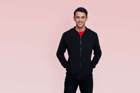 Frontal image of a smiling handsome young brunette man in dark blue jumper and jeans over pink background.の写真素材