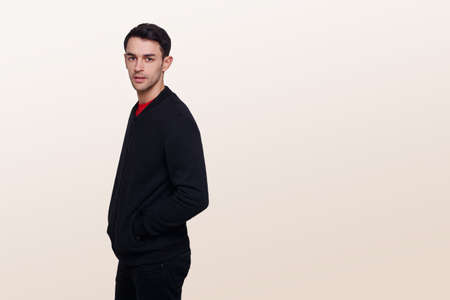Portrait of a young man in dark blue jumper and jeans, with a hood on his head, isolated light beige background.の写真素材