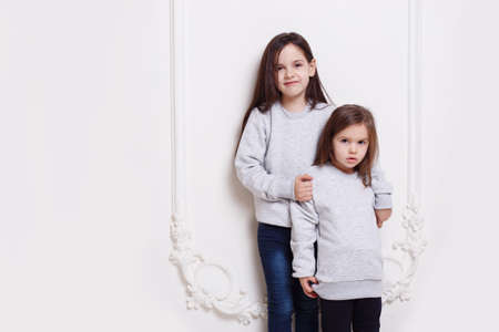 Two adorabile sisters posing together on white background, smiling and looking at camera.の写真素材