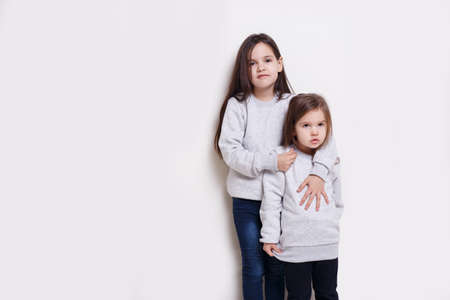 Two adorabile littel girl in sweater and jeans, posing together on white background, smiling and looking at camera.の写真素材