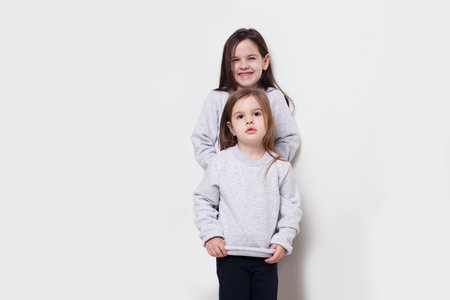 Two adorabile littel girl in sweater and jeans, posing together on white background, smiling. Posing in studio.の写真素材