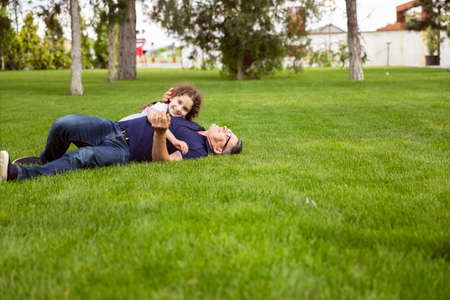 Full length image of a niece hugs her grandfather in the park on a sunny day, they lie on the green grass.の写真素材
