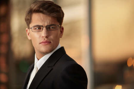 Portrait of a handsome businessman in eyeglasses and black suit., sunset background.の写真素材