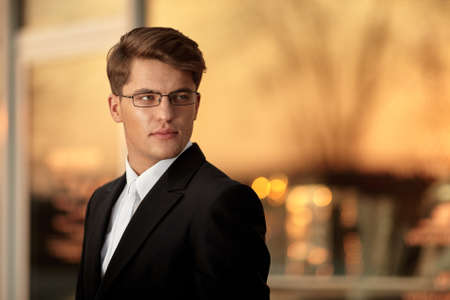 Portrait of a handsome businessman in eyeglasses and black suit, sunset background. Space for text.の写真素材