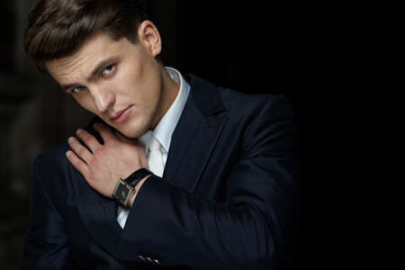 Closeup portrait of a handsome businessman posing in black suit, wear watch on his hand, isolated black background.の写真素材