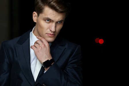 Front portrait of a handsome businessman posing in black suit, wear watch on his hand, isolated black background.の写真素材