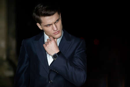 Elegant businessman posing with crossed arms in black suit, wear watch on his hand, isolated black background.の写真素材