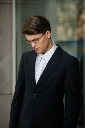 Profile portrait of a handsome brunette businessman in eyeglasses and black suit and white tie and shirt, looking down.の写真素材