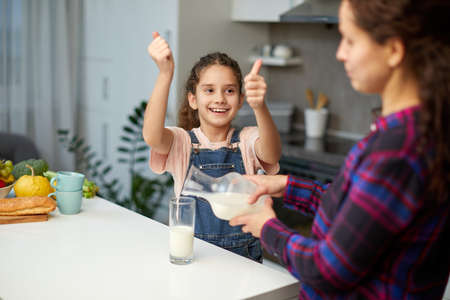 The happy little girl shows the thumbs having breakfast together in the kitchen.の写真素材
