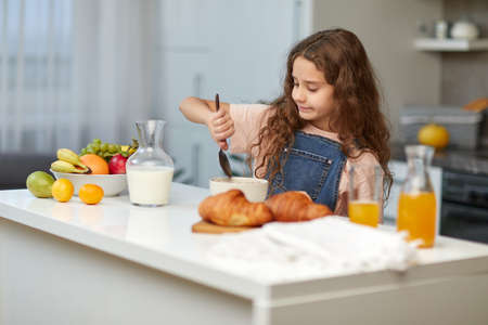 Adorable little girl with curly hair eating cereals healthy breakfast on the kitchen.の写真素材