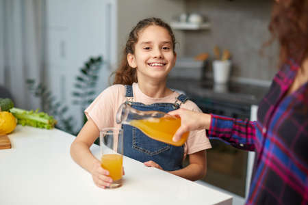 Portrait of a mom pours her cute daughter orange juice for breakfastの写真素材