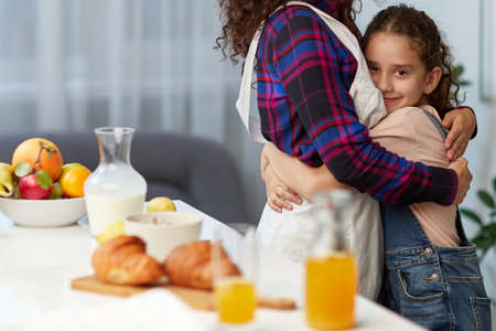 Closeup portrait of a mom embrace her cute daughter in the kitchen near table, take breakfast together.の写真素材
