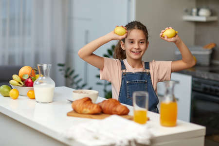 Cute girl holding and shows of lemons in kitchen.の写真素材