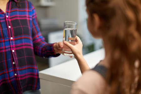 Cropped image of a little girl holding a glass of water in the kitchen with the young mother.の写真素材