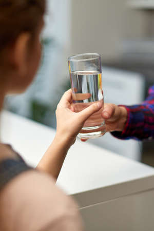 Cropped image of a hand little girl holding a glass of water in the kitchen with the mother.の写真素材
