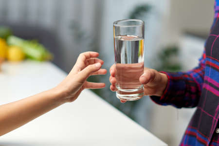 Frame image of a little girl hand holding a glass of water in the kitchen with the young mother.の写真素材