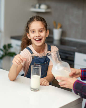 Portrait of a mom pours her cute laughing daughter, milk in glass.の写真素材