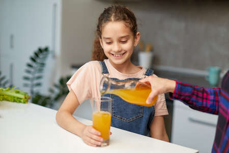 Closeup portrait of a mom pours her cute daughter orange juice for breakfast.の写真素材