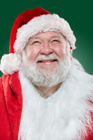 Closeup view of a happy laughing Santa Claus dressed in a red coat and a hat, looking up, isolated green background.の写真素材