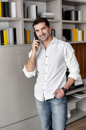 Businessman talking on stationary phone in office standing behind workplace, looking at camera.の写真素材