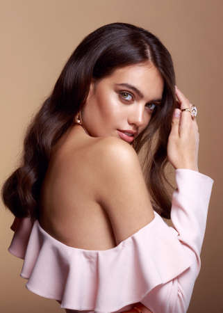 Closeup image of a sensual woman with bare shoulders, brown wavy hair, isolated brown background.の写真素材