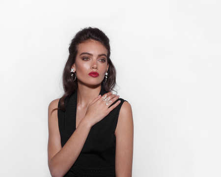 Brunette young woman dressed in black dress, with makeup, wears luxurious jewelry, on a white background.の写真素材