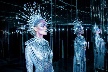 Fashionable young woman with creative makeup wearing futuristic costume, reflection in mirror.の写真素材
