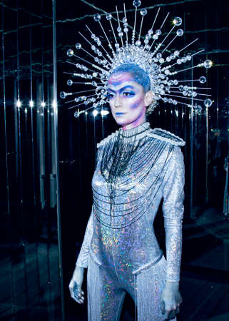 Fashionable young woman with creative makeup wearing futuristic costume, reflection in mirror.の写真素材
