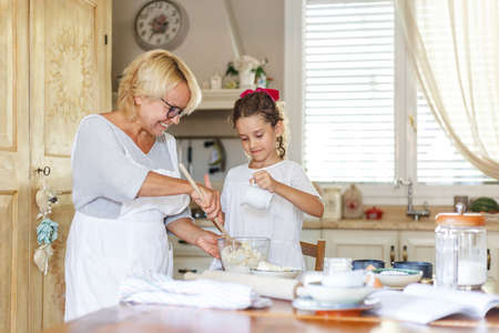 Happy grandmother and adorable little curly granddaughter in the kitchen, they are preparing together.の写真素材