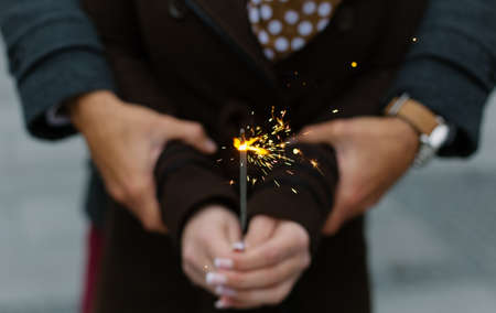 Closeup of a couple standing outdoors, holding Christmas sparkler