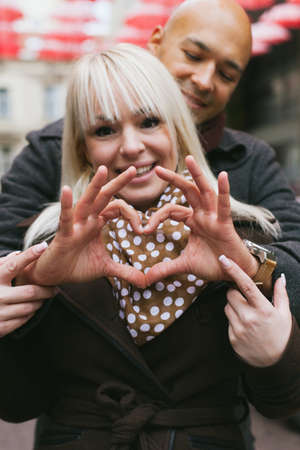 Man making heart shape with hands over his girlfriend while she looks at the cameraの写真素材