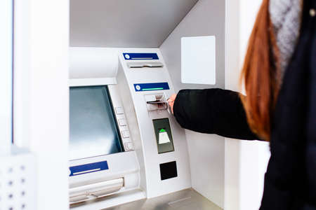 Closeup of girl holding shopping bags withdrawing money from ATM machineの写真素材
