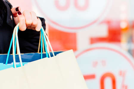 Closeup of woman holding shopping bags in front of store window with copy space