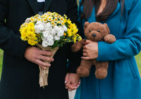 Concept of Valentines Day. Closeup of couple holding hands. Woman holding teddy bear and man holding flowersの写真素材