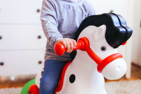Cute kid having fun at home. Closeup of little girl riding toy rocking horseの写真素材