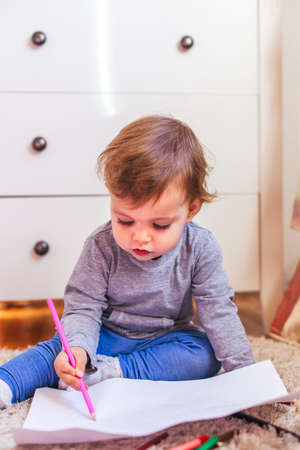 Beautiful little girl sitting on the floor and paintingの写真素材