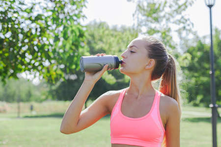Young woman taking a break to drink some water during the workout outdoor with copy space