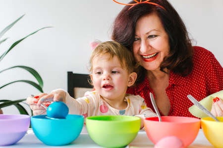 Easter concept. Little girl and grandmother coloring eggs for easterの写真素材