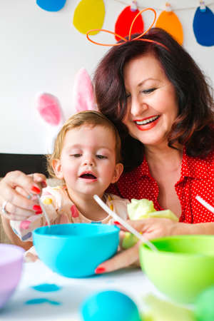 Easter concept. Grandmother helping little girl to paint eggs for easterの写真素材