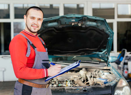Portrait of a mechanic writing on a clipboard in front of his carの写真素材