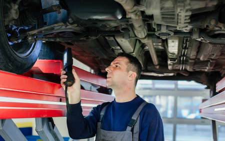 Mechanic examining car using flashlight in auto service
