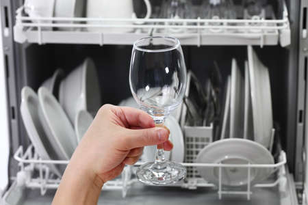 dishwasher, open and loaded with dishes, man hand taking out clean wine glass, after washingの写真素材