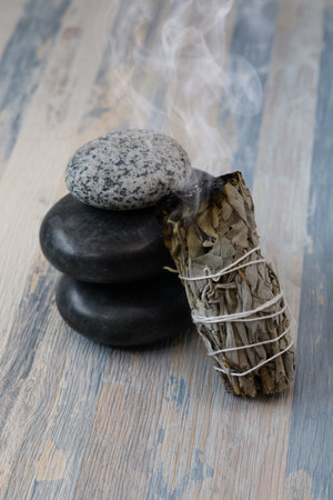 A  lit white sage smudge stick beside the stones. for meditation, healing, and spiritual room cleansing.の写真素材