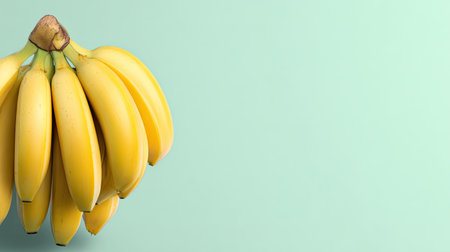 A stunning bunch of fresh yellow bananas against a soft light green background, ideal for promoting healthy eating, nutrition, and vibrant food concepts.の素材