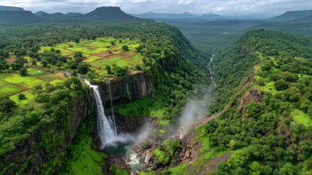 Breathtaking view of a majestic waterfall flowing into a serene river amidst a lush green landscape, surrounded by rolling hills and a vibrant forest.の素材