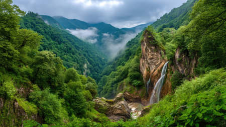 Captivating view of a beautiful waterfall cascading down rocky cliffs, framed by thick greenery and scenic mountain ranges shrouded in mist.の素材
