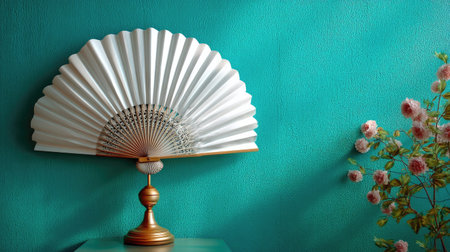 A stunning white fan beautifully positioned against a rich turquoise wall, accompanied by soft pink flowers, creating a serene and sophisticated decor.の素材