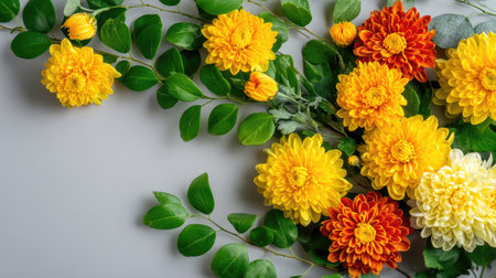 A stunning flat lay showcasing a vibrant mix of yellow and orange flowers alongside fresh green leaves, set against a soft gray background.の素材