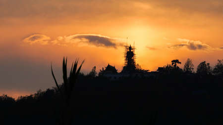 Thailand, Chiangmai Province, Wat Phra That Doi Kham, Monk scales web of bamboo scaffolding around unfinished Buddha, Sunsetの素材